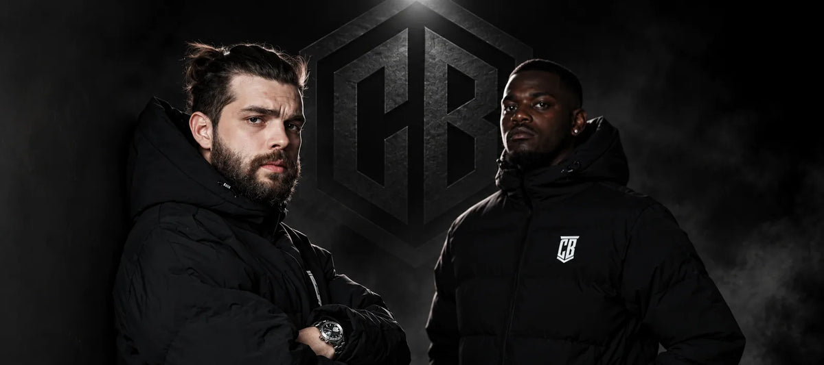 Two men in black CB puffer jackets in front of the CB logo