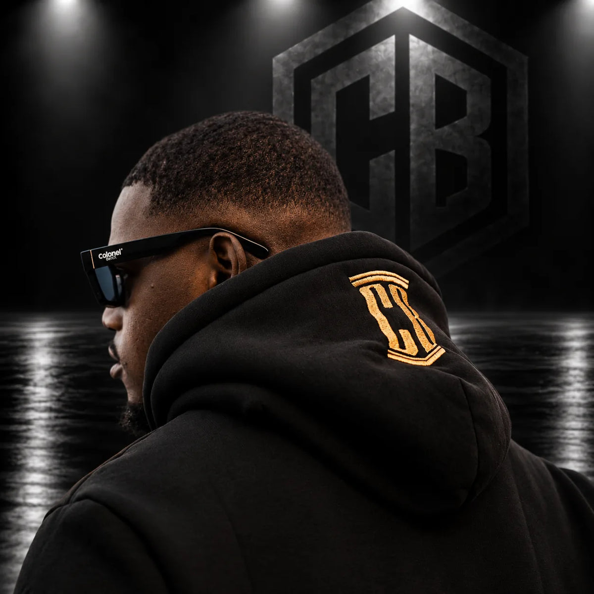 Gold CB embroidery on the hood of a black Colonel Bench hoodie, studio shot