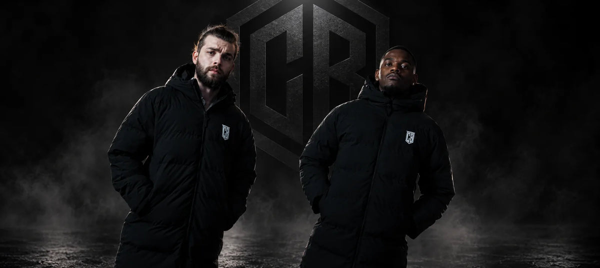 Two men in black long Colonel Bench parkas in a smoky studio with the CB logo